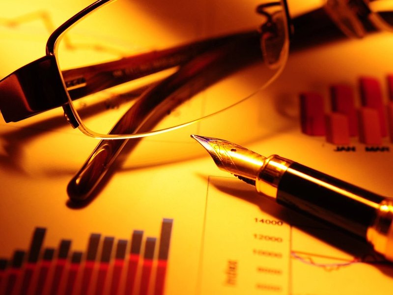 pair of glasses and a pen on a table with business charts